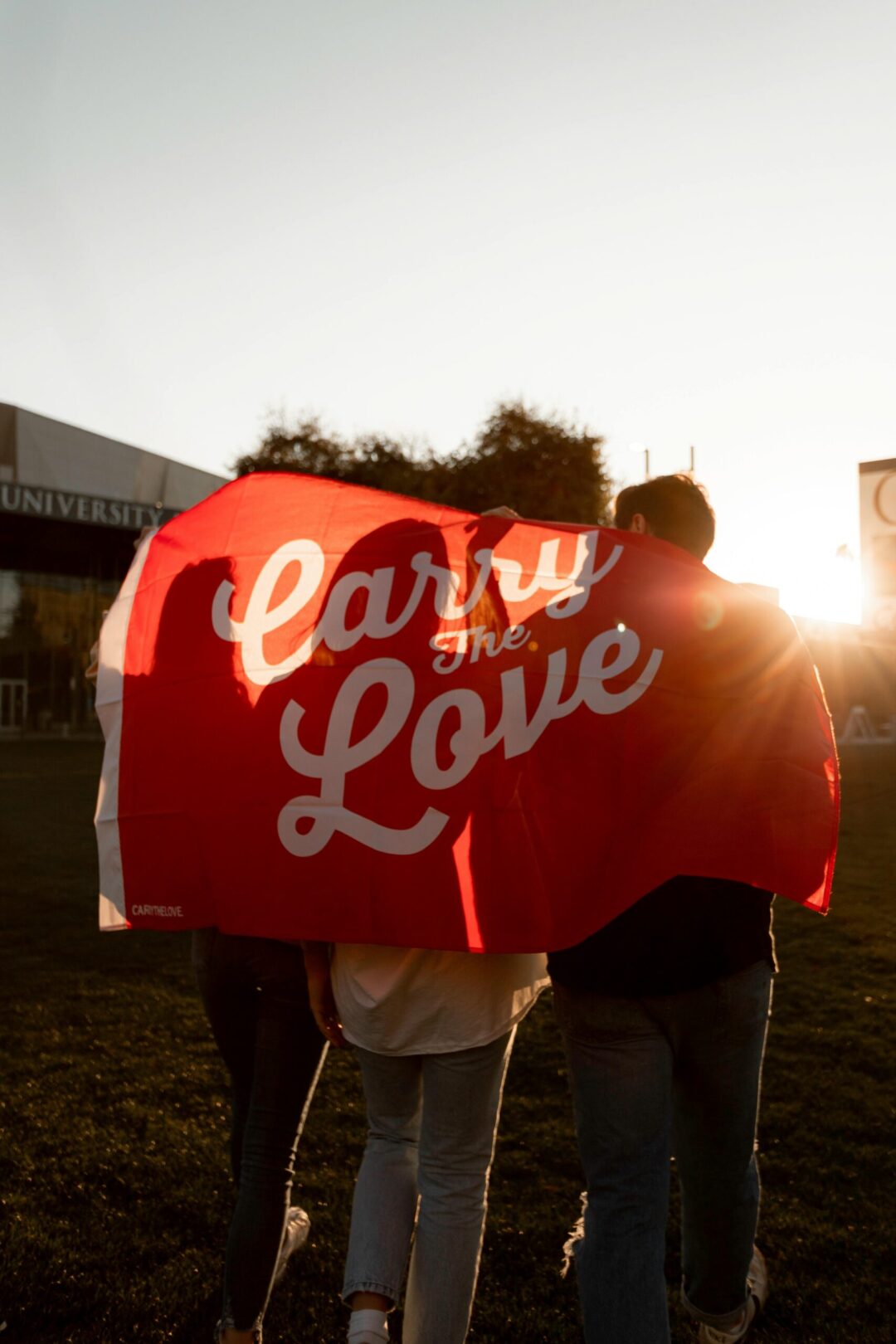 Group of friends walking with 'Carry the Love' banner during sunset outdoors.