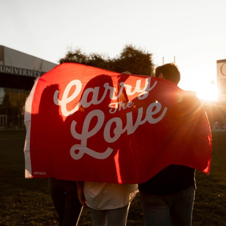 Group of friends walking with 'Carry the Love' banner during sunset outdoors.