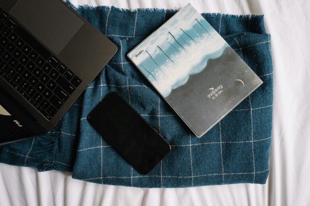 Flat lay of a laptop, smartphone, and notebook on a checkered blanket, creating a modern cozy vibe.