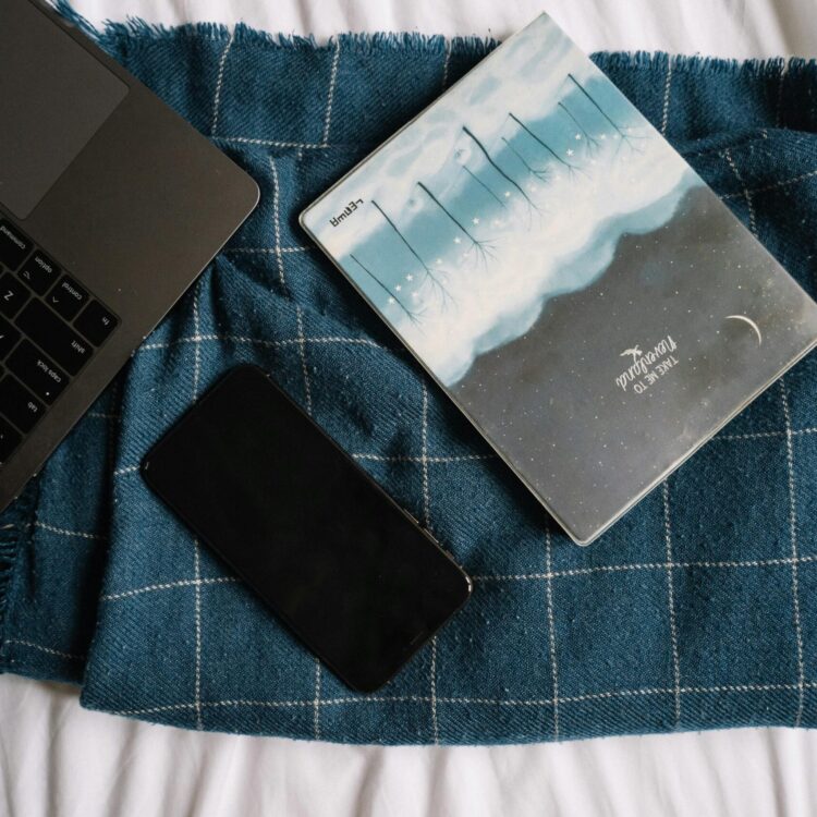 Flat lay of a laptop, smartphone, and notebook on a checkered blanket, creating a modern cozy vibe.