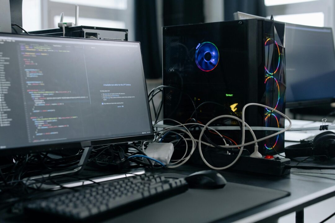 A modern workspace featuring a computer monitor with code, a PC tower, and peripherals.