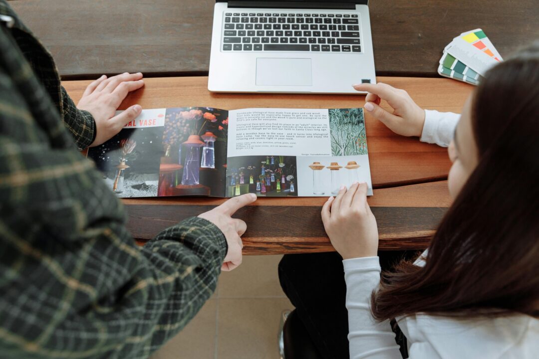 Two people reviewing a design brochure at a collaborative workspace with a laptop.