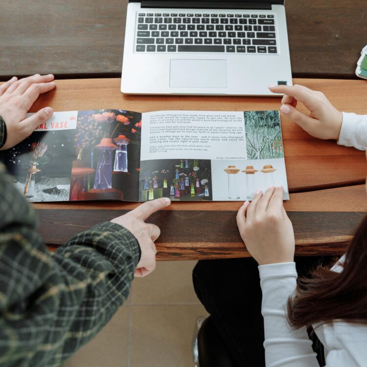 Two people reviewing a design brochure at a collaborative workspace with a laptop.